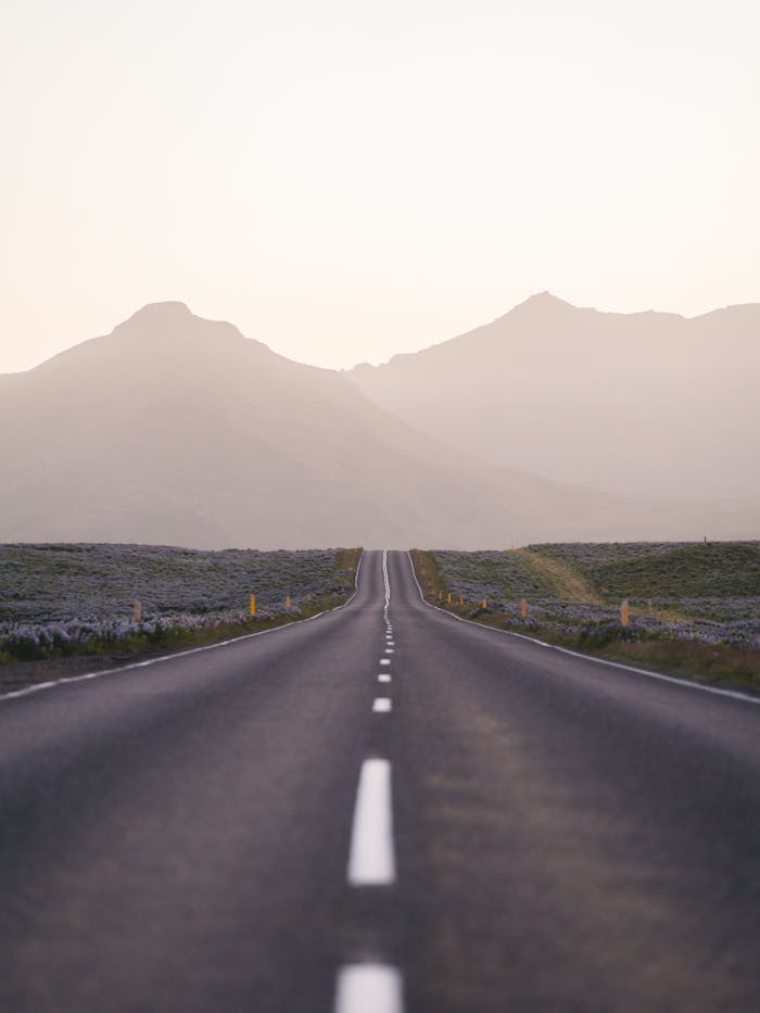 A picturesque view of an empty road leading towards distant mountains under a soft dawn sky in Iceland.